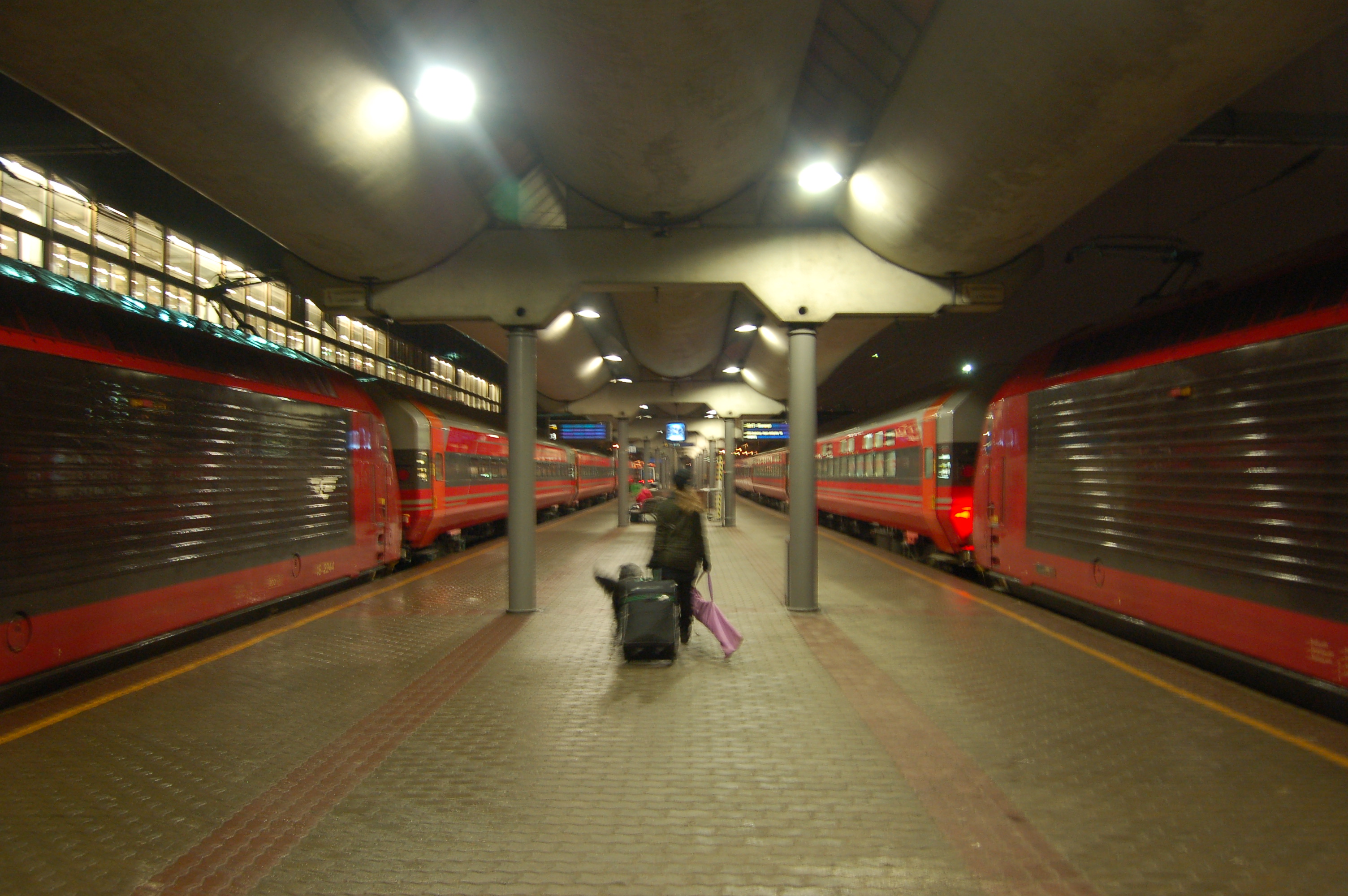 Dwa pociągi nocne stojące przy peronach dworca Oslo S wieczorem, oświetlone wnętrza wagonów.